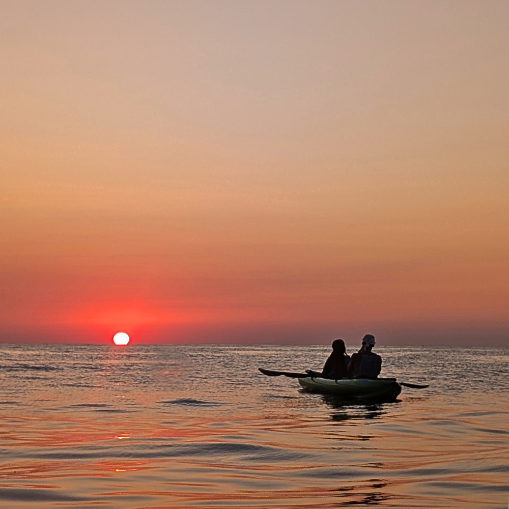 Couple watching the sunrise from a kayak in Malta on calm morning water.
