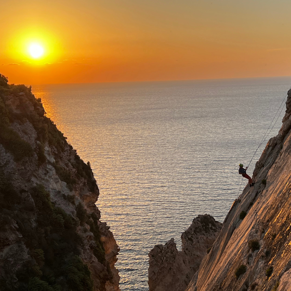 Abseiling at sunset in Malta with warm orange light illuminating the cliffs