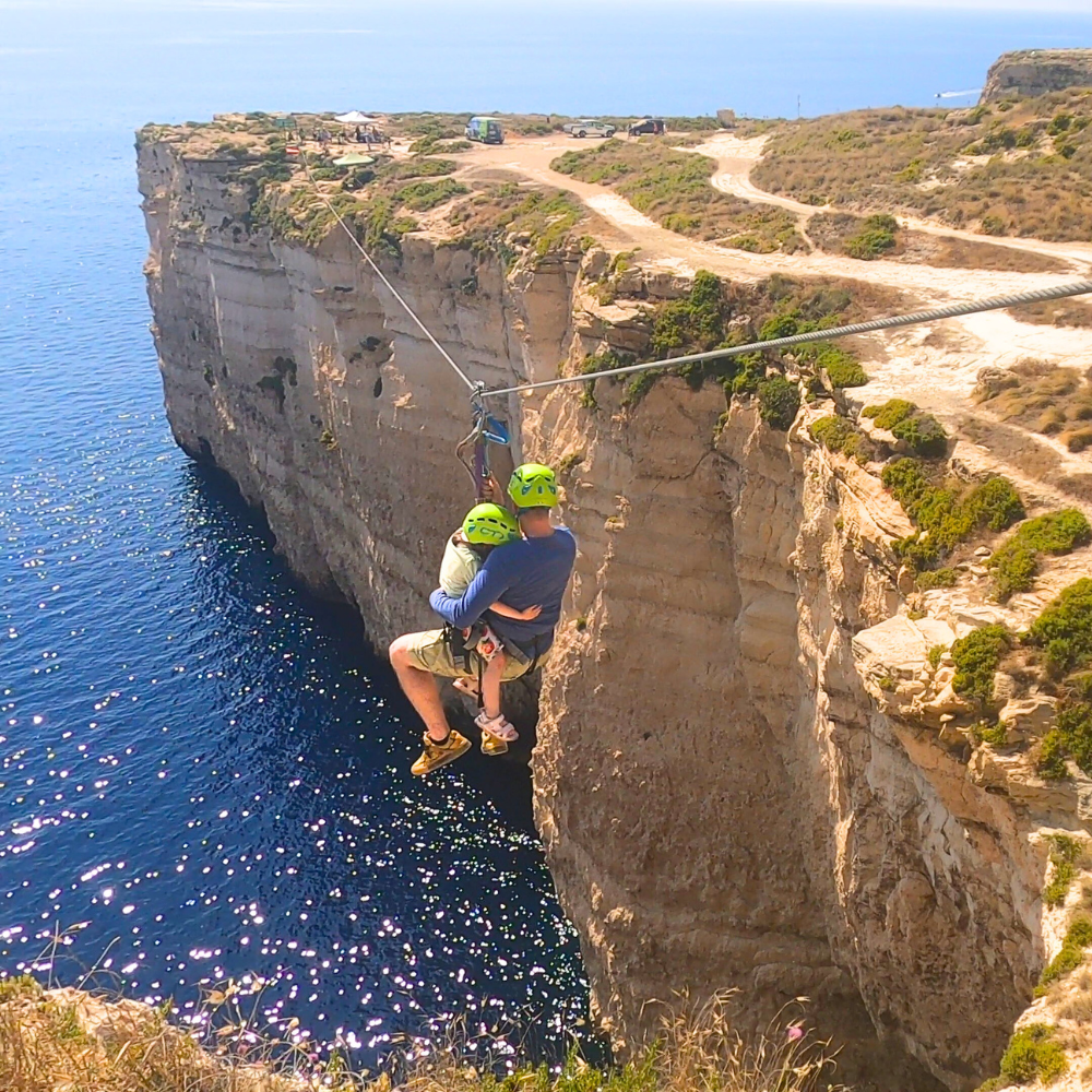 Father and daughter riding the zipline in Malta together, secured with harnesses.