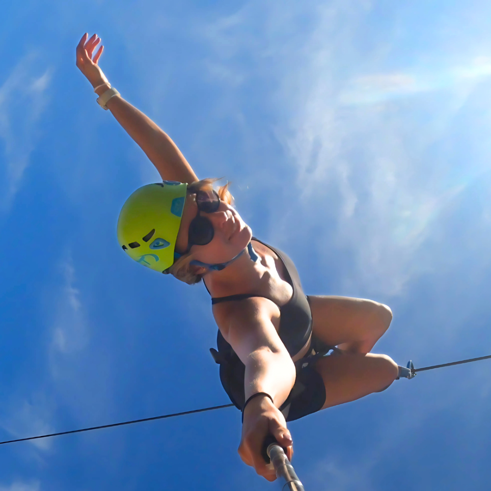Girl riding a zipline upside down, hanging securely with harness and trolley.